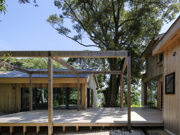 開放的な軒下空間（非断熱設計）を特徴とする母屋（右）と室内環境を意識した断熱設計の離れ（左）を繋ぐウッドデッキを新設。その杭が雨水を地中に浸透させる役割を果たす。見ていただくと先が黒く焼かれていることが分かる（撮影/八代写真事務所）