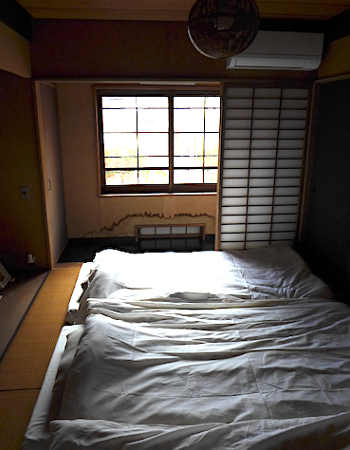 床が斜めの廊下。よく見るとドアの枠も斜め。壁に赤い光が映っているのは、廊下の右の部屋に差し込んだ光がカーペットに反射したもの。狭い廊下は雁木にも見える