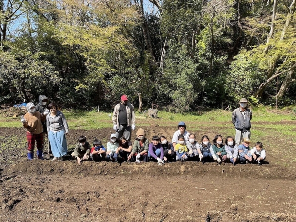 よく耕された畑の畝うねの前で、一列になって笑顔で写る、地域の子どもたちと難民の方々。アルペなんみんセンターの一角で、農作業を一緒に行っているそうだ