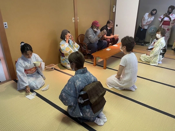 和室で地域の方々と茶道のお茶会を体験する難民の方々。女性の難民の方々は着物や浴衣を着て正座で、男性陣は座椅子に腰掛けながら、抹茶を振る舞われている