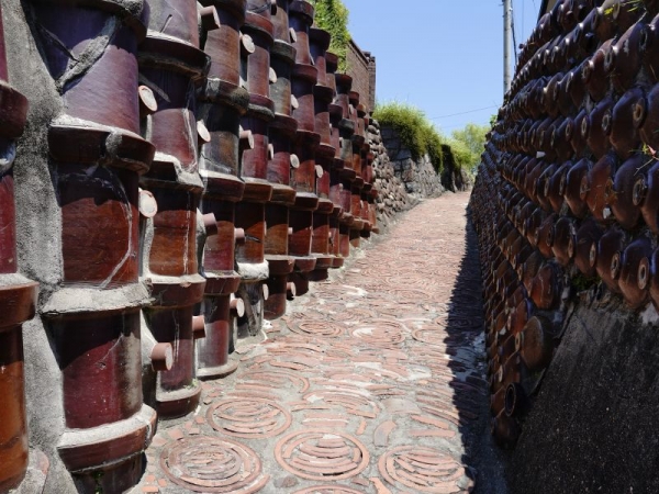 昭和初期ごろに最も栄え、陶器工場が並んでいたまちなみのことを「やきもの散歩道」と名付け、観光スポットに。カフェや雑貨店などがオープンするなか、写真の明治期の土管と昭和初期の焼酎瓶が壁面をおおった“土管坂”や、民家で陶器の廃材利用した箇所があるなど、歴史ある焼き物のまちを感じられる（※観光の際は、私有地への無断侵入など住民への配慮を）