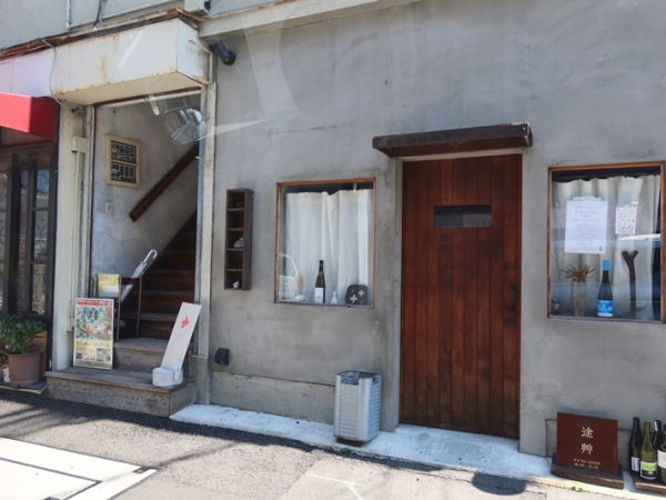 オフィスのあるビルの入口で山居さん。ちなみに１階には十二庵キッチンという飲食店が入り、３階はコワーキングスペース、４階はライブラリーとなっている（筆者撮影）