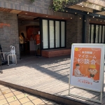 ウッドデッキ前に設置されたオレンジ色のポスター。LIFULL HOME'S のキャラクターホームズ君と女性が正面を向いた写真とともに、「本日開催！マイホーム相談会」と書かれている。